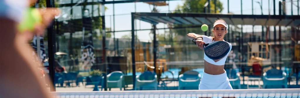 Lady in white hitting a tennis ball with a Padel racket